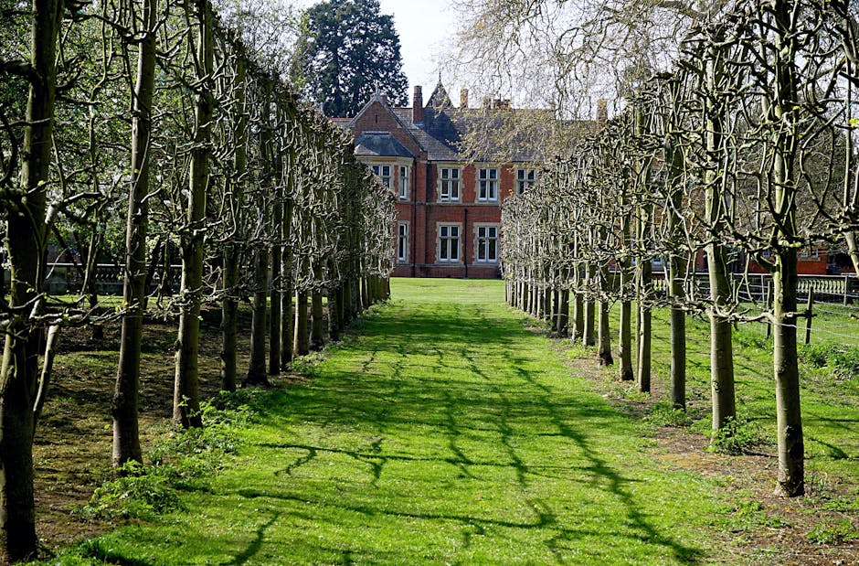 The image depicts a historic red-brick mansion with a symmetrical faÃ§ade, multiple small windows, and decorative architectural details, set against an overcast sky. In the foreground, a formal garden